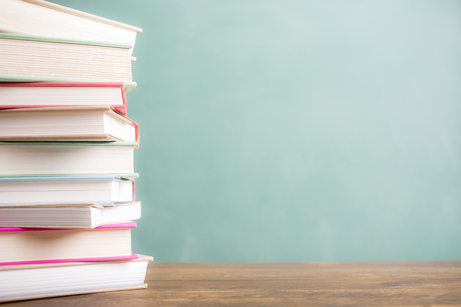 It's back to school time!  A large stack of textbooks to side makes frame composition.  The pile of objects lies on top of a wooden school desk with a green chalkboard in the background.  The blank blackboard in the background makes perfect copyspace!  Education background themes.