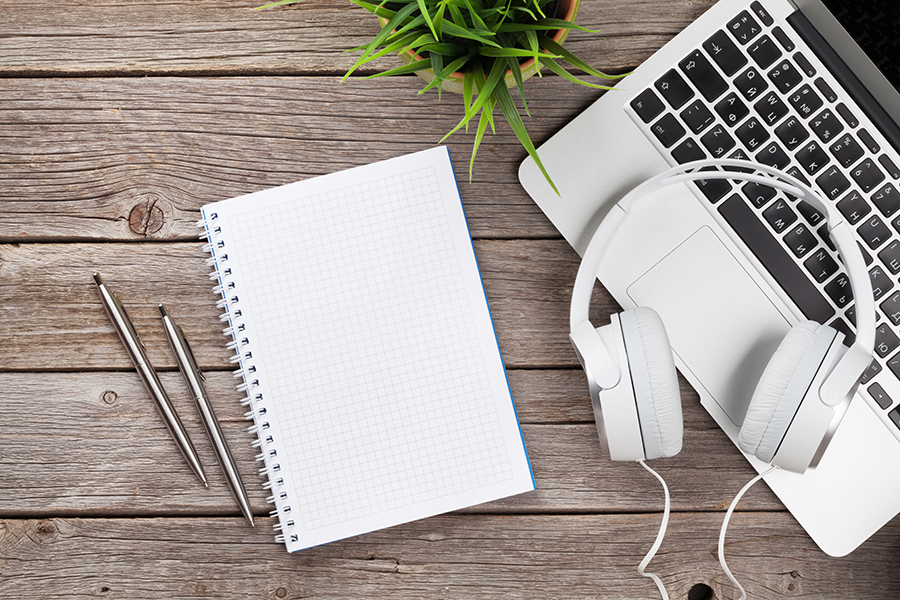 Headphones over laptop and notepad on wooden desk table. Music concept. Top view with copy space